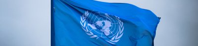 The United Nations flag with a white atlas flys on a flag pole before a grey sky