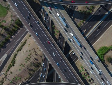 An aerial view of a motorway junction showing the roads crossing each other in an attractive pattern. Some roads are straight, others are curved. Each has multi coloured cars on it.