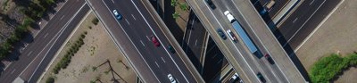 An aerial view of a motorway junction showing the roads crossing each other in an attractive pattern. Some roads are straight, others are curved. Each has multi coloured cars on it.