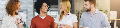 Two men and two women standing in office holding mugs and chatting