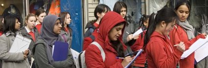 A group of female students with clipboards are walking down a high street taking notes of what they can see for their Geography fieldwork