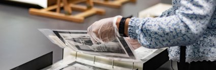 A researcher wearing archival gloves viewing historic photographs in a folder