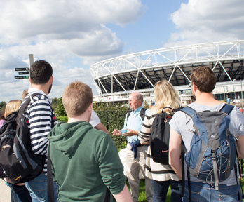 A group of teachers standing outside the London 2012 Olympic stadium in Stratford, London. They are being guided by a fieldwork expert in how to lead fieldwork for schools in the area.