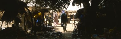 A man walks under a canopy covering a marketplace into the sunlight 