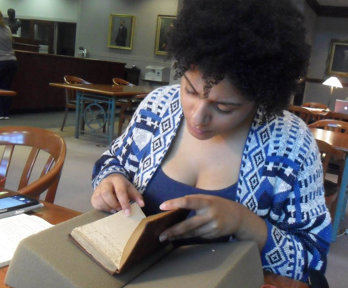 Person sat at table and carefully looking through an old hardback notebook with hand written notes. 