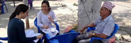 Three people sat on chairs in a circle conversing and taking notes. 