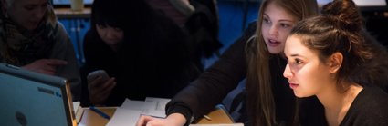 Two school pupils in a class sit looking intently at a laptop.