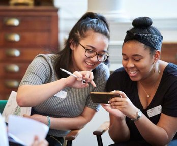 Two female geography ambassadors looking at a mobile phone and smiling