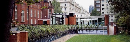 Exterior of the Royal Geographical Society from the garden, showing redbrick building and modern glass Pavilion