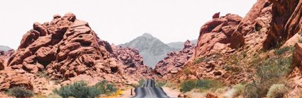 A Nevada road stretching out into the distance, the yellow central lines weaving slightly where the road bends. The road has rocky outcrops either side and in the distance