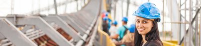 Woman with long, dark hair smiling and wearing blue hard hat in construction setting