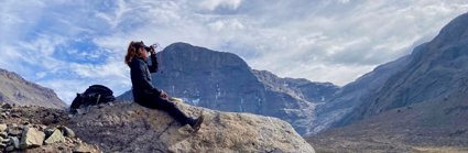 Person sat on a rock looking out at a mountainous landscape in Chile. The person is holding a compass and has a rucksack beside them. 