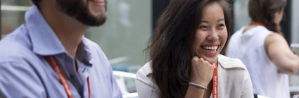 An Asian woman and white man sit next to each other smiling while wearing professional clothing and lanyards.