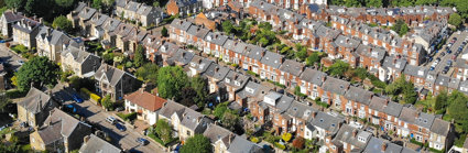 An aerial view of a residential area, with orange houses with grey roofs and small green gardens. The suburban area stretches off into the distance, with a few high rise tower blocks also in the view.