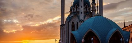 The sun is setting over ornate Russian buildings, which have arched windows, thin towers and turrets