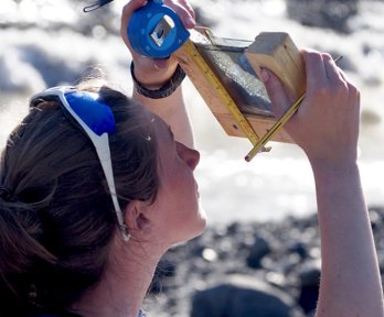 A person wearing sunglasses on their head holding a tape measure and sample up to the light. 