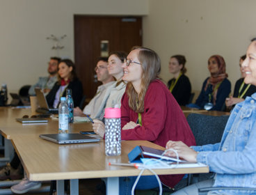 A group of people sit in a seminar room at the RGS-IBG Annual Conference. They are listening to a discussion, some of them are smiling.