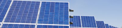 Blue solar panel sheets laid out in a green field. The sun is shining and the panels are casting a shadow on the grass