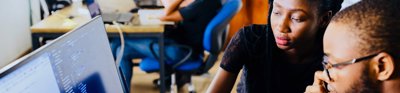 A Black man and woman sat looking at a laptop in an office setting. 