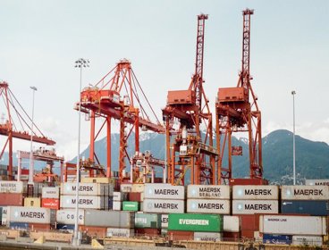 Shipping containers on a boat, with red cranes at the side ready to lift them on and off. 