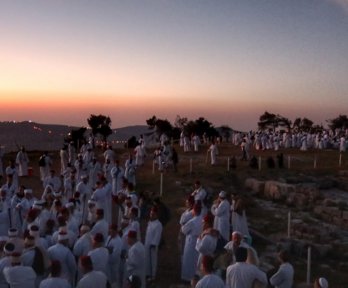 A large group of people gathered for a ceremony on a mountaintop as the sun is setting. 