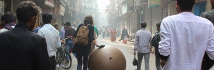 Streetscene with people and large bronze ball sculpture being wheeled along the street