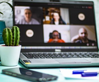 A cactus, mobile phone, laptop showing open conference call, and blue pen