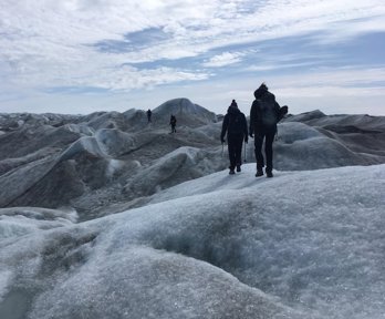 Four people walking across an undulating glacial landscape carrying equipment. 