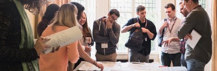 Group of people standing around a table spread with lots of maps.