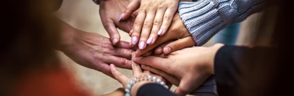 A group of people laying their hands of top of each others hands to indicate a team