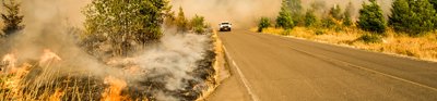 Car on straight road with smoke from fire behind 