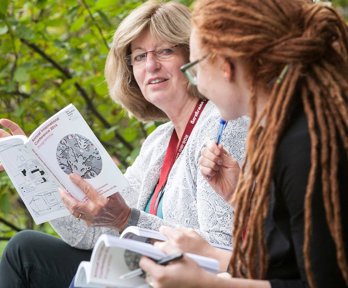 Two white women having a conversation while holding printed conference programmes