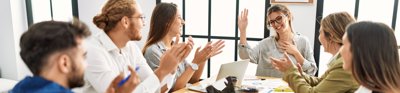 Group of people sat around a table clapping and congratulating colleague