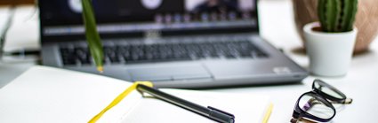 A yellow notebook open in front of a laptop, pen, black glasses