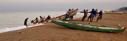 Group of people on a beach pulling a rowing boat onto the shore from the water. 