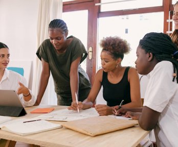 People standing and sitting around a desk with papers and laptop