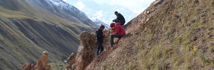 Three researchers sit on a sloping valley side writing in notebooks. 