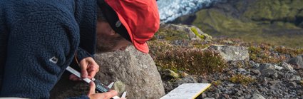 Person measuring the size of a mark on the side of a rock in a cold rocky landscape.