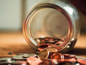 Close-up photo of assorted coins coming out of a glass jar 