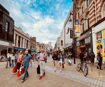 A high street shopping area, with people walking along carrying bags of shopping