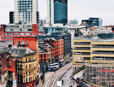 Manchester city Centre, showing buildings, retail and a tram line. The Arndale shopping Centre can be seen, and there is a tram on the lines