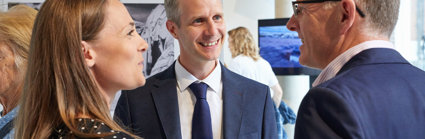 Three people in professional attire smiling and talking in a Society exhibition.