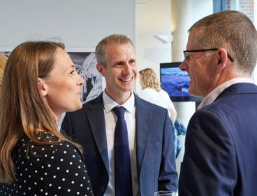 Three people in professional attire smiling and talking in a Society exhibition.